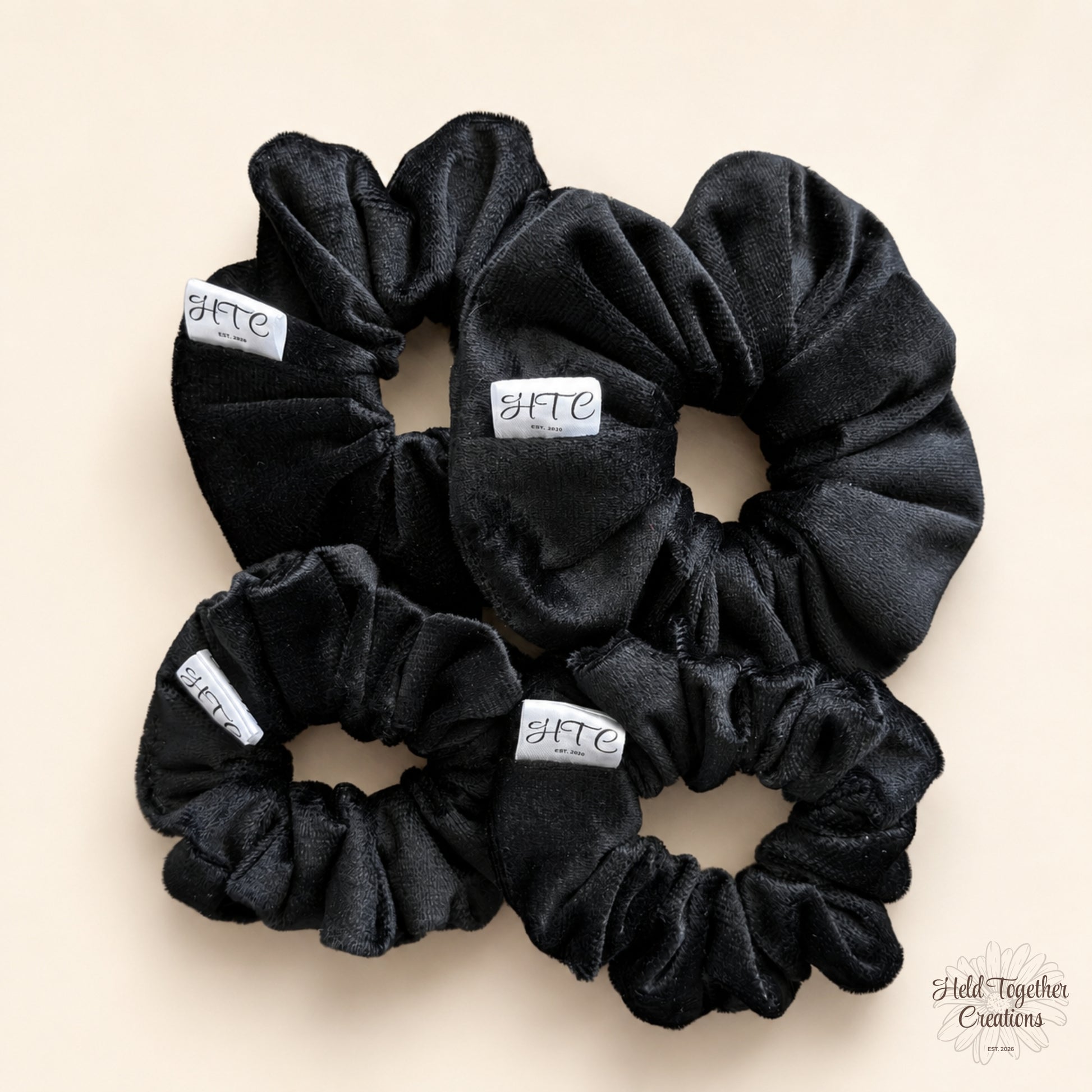 Black velvet handmade scrunchie with white HTC label on a warm neutral background.