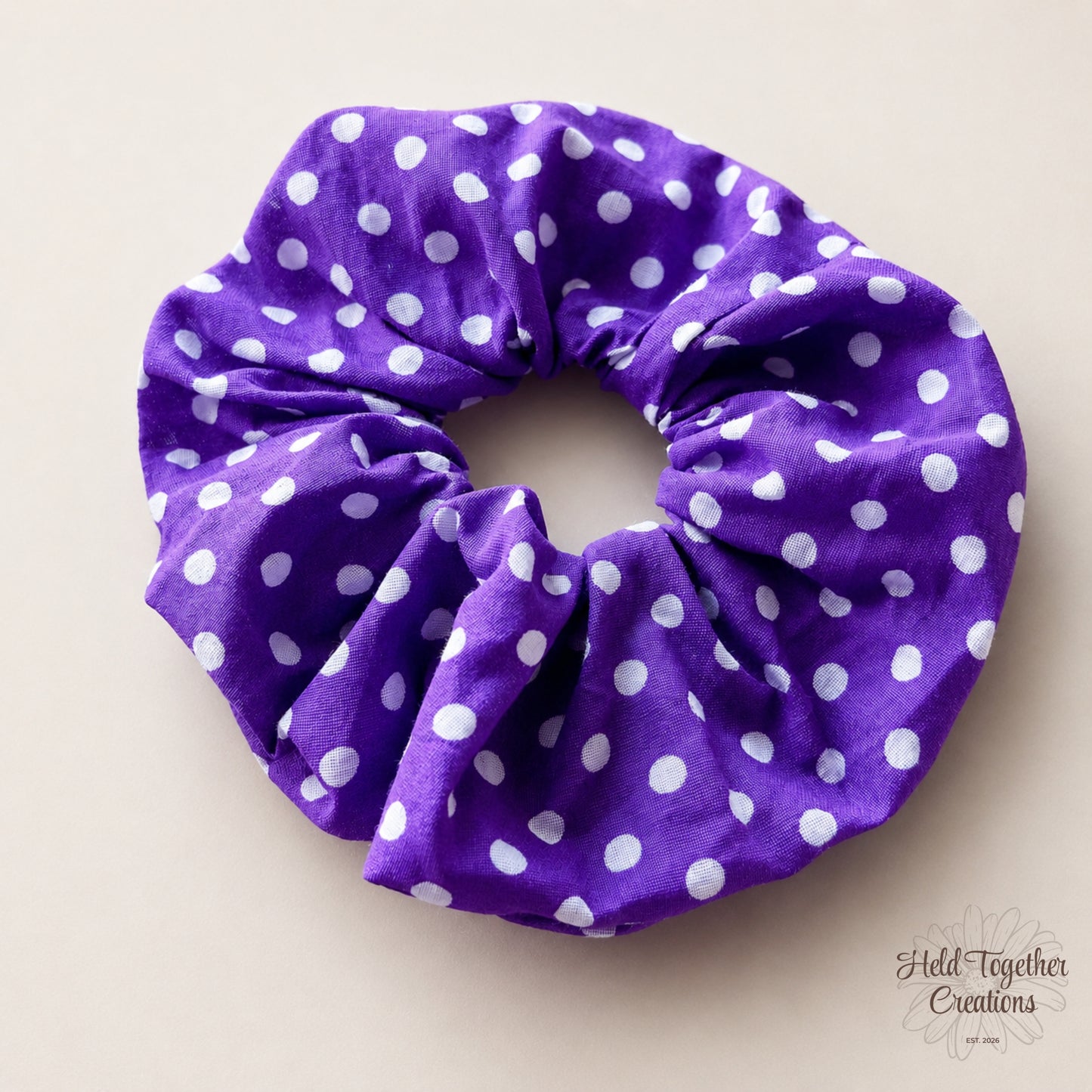 Purple scrunchie with white polka dots on a beige background