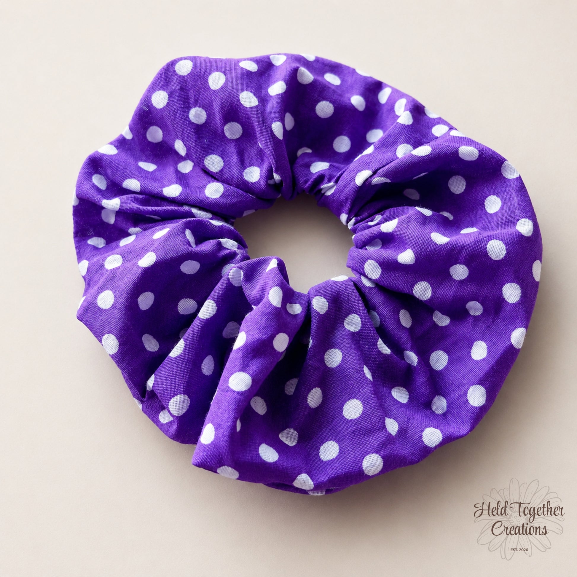 Purple scrunchie with white polka dots on a beige background