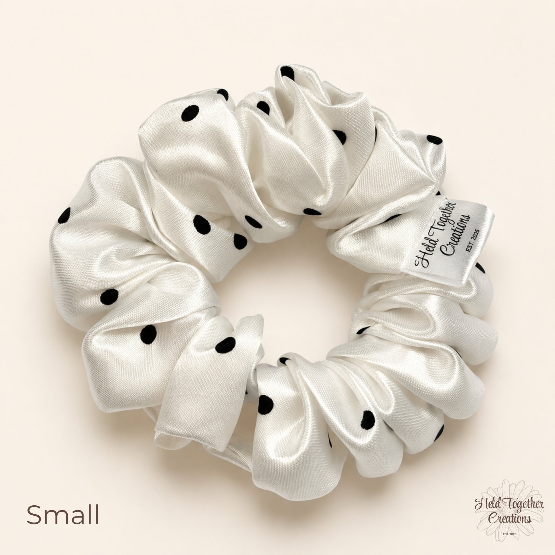 Small white satin scrunchie with black polka dots on neutral background.