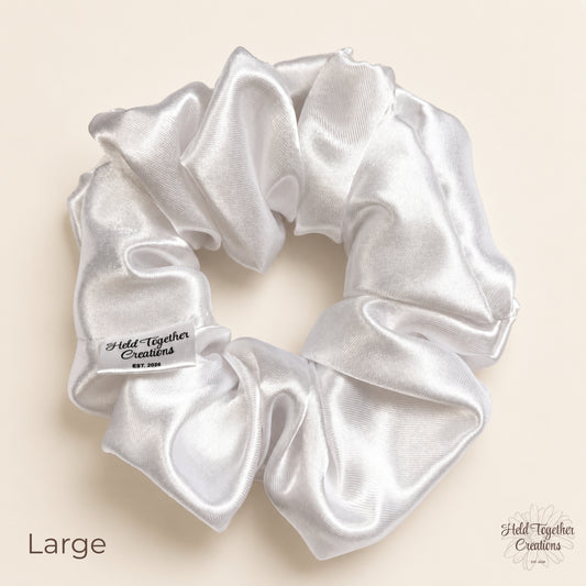 Large white satin scrunchie on a warm neutral background with Held Together Creations label visible.