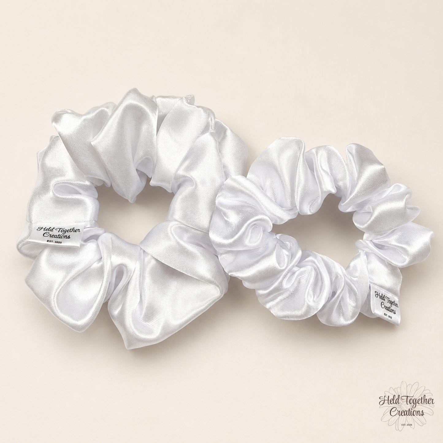 Small and large white satin scrunchies side by side on a warm neutral background.
