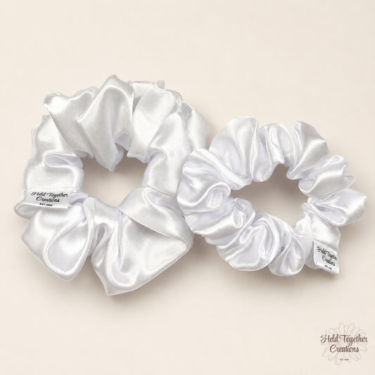 Small and large white satin scrunchies side by side on a warm neutral background.