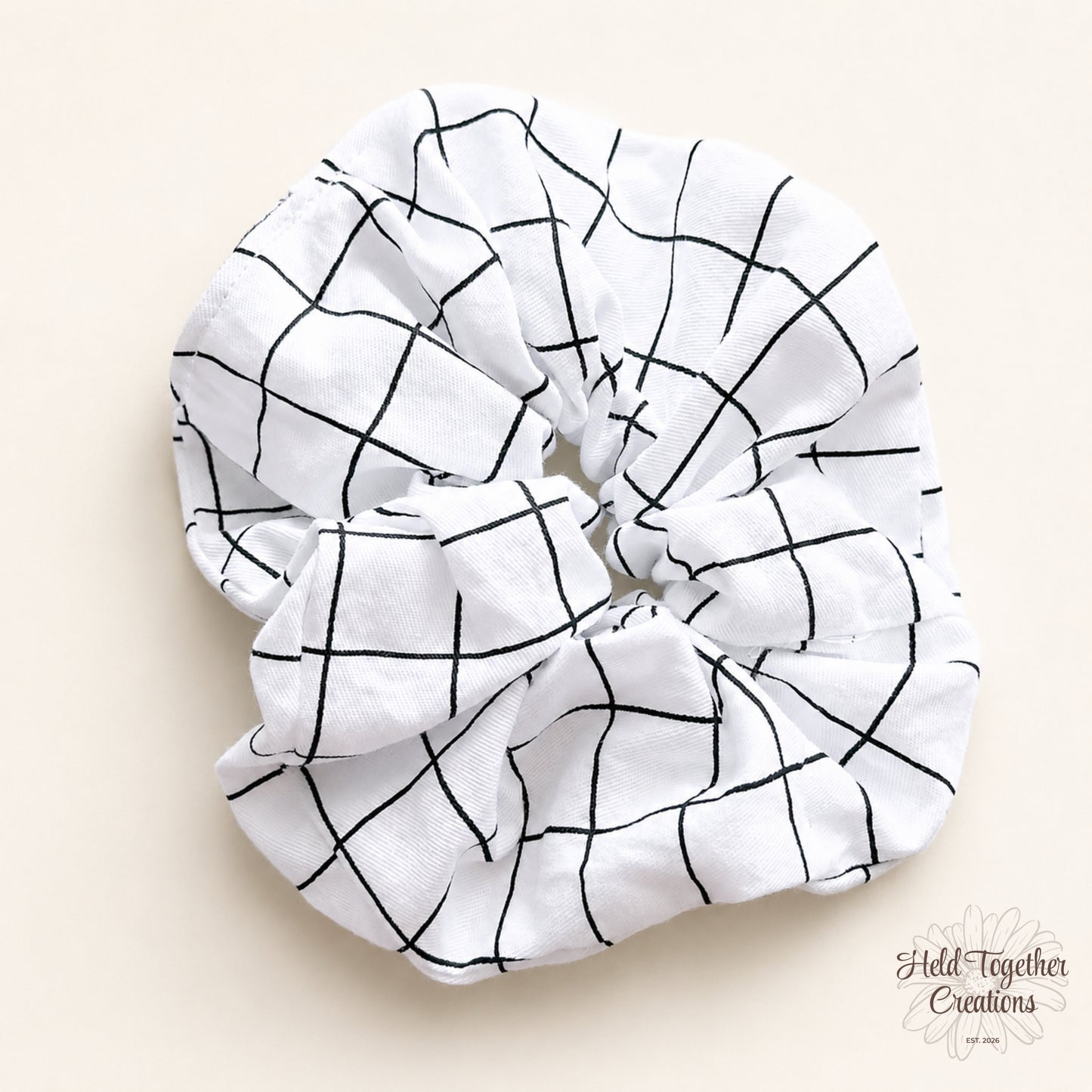 White handmade scrunchie with black grid pattern on a soft neutral background.