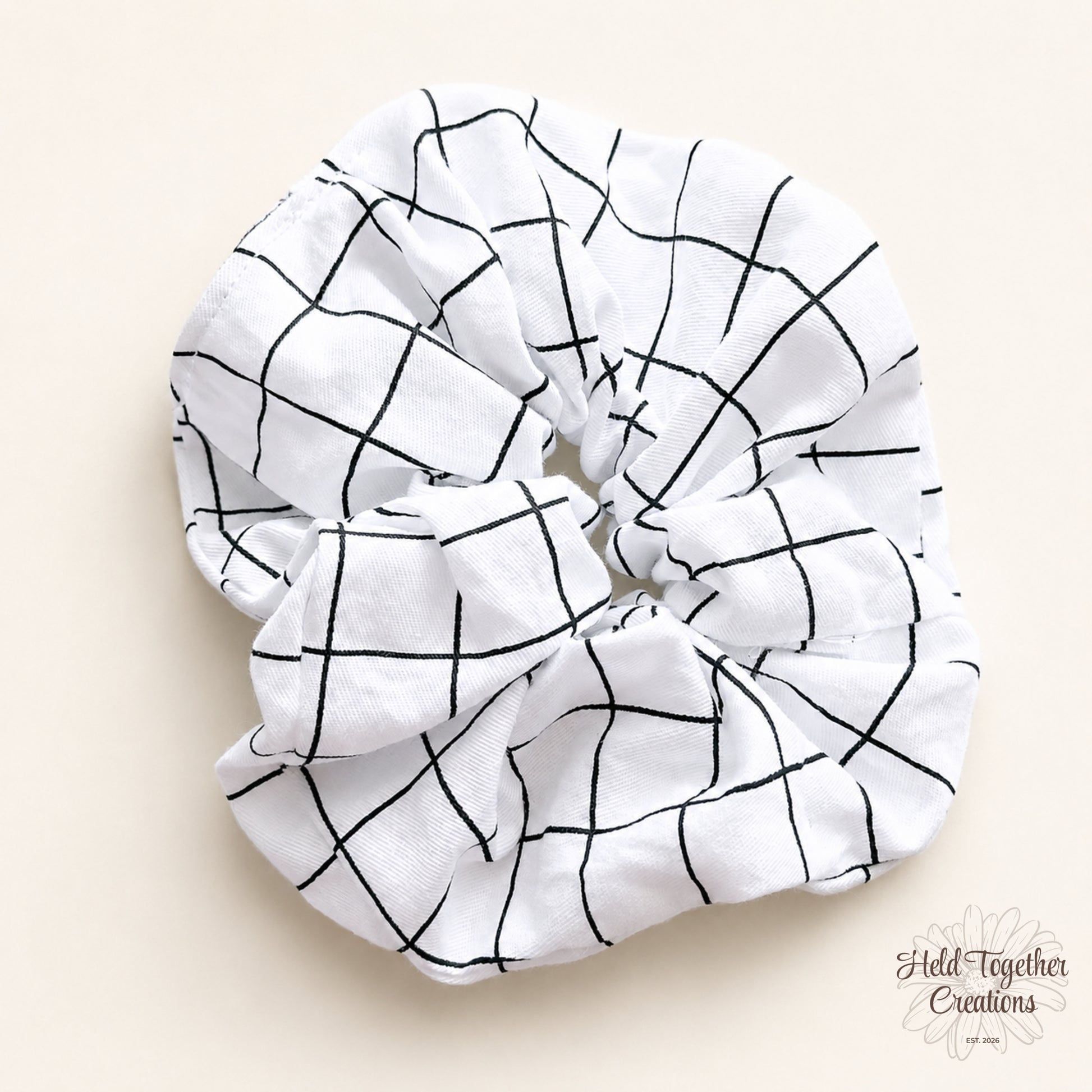 White handmade scrunchie with black grid pattern on a soft neutral background.