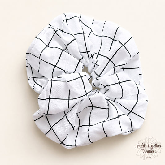 White handmade scrunchie with black grid pattern on a soft neutral background.