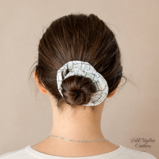 White handmade scrunchie with black grid pattern on a soft neutral background.