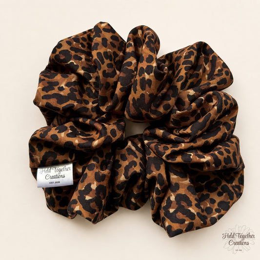 Leopard print XL scrunchie flat lay with Held Together Creations tag on warm ivory background.