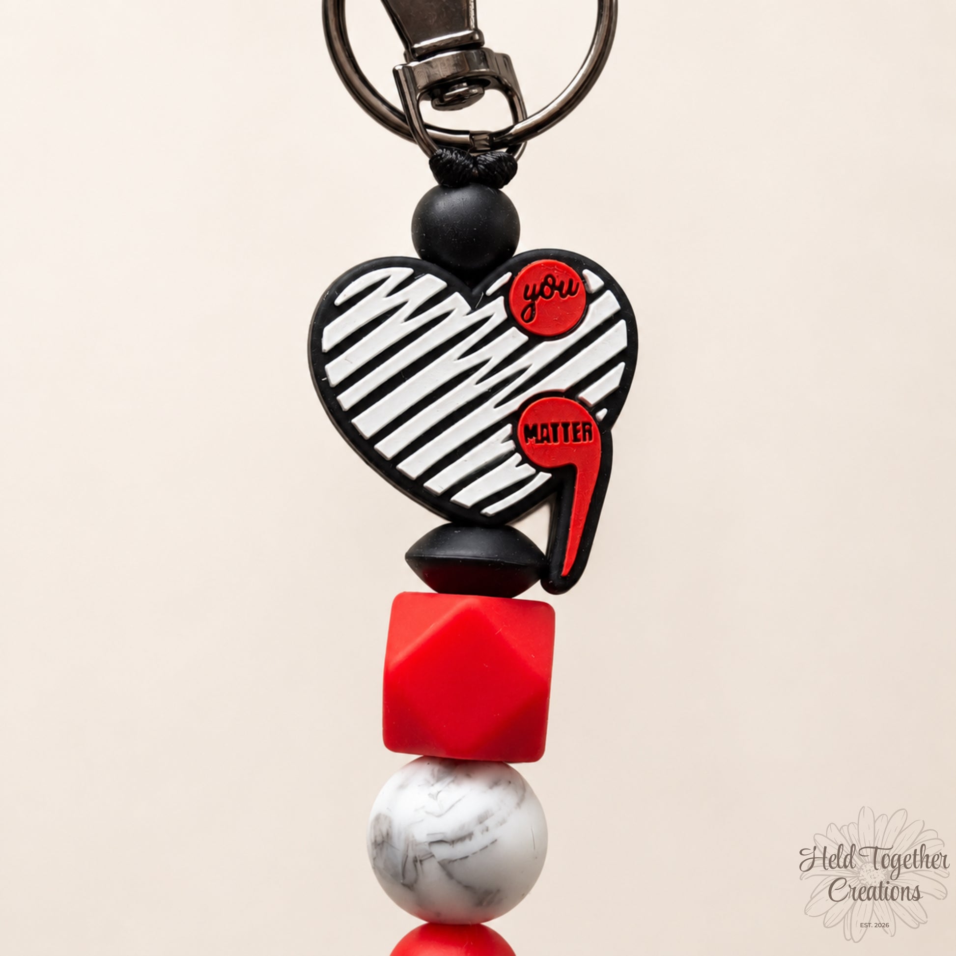 Heart-shaped keychain with red and black elements on a beige background