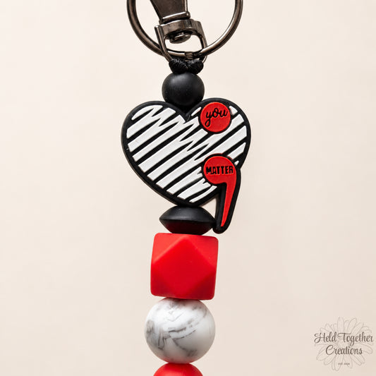 Heart-shaped keychain with red and black elements on a beige background