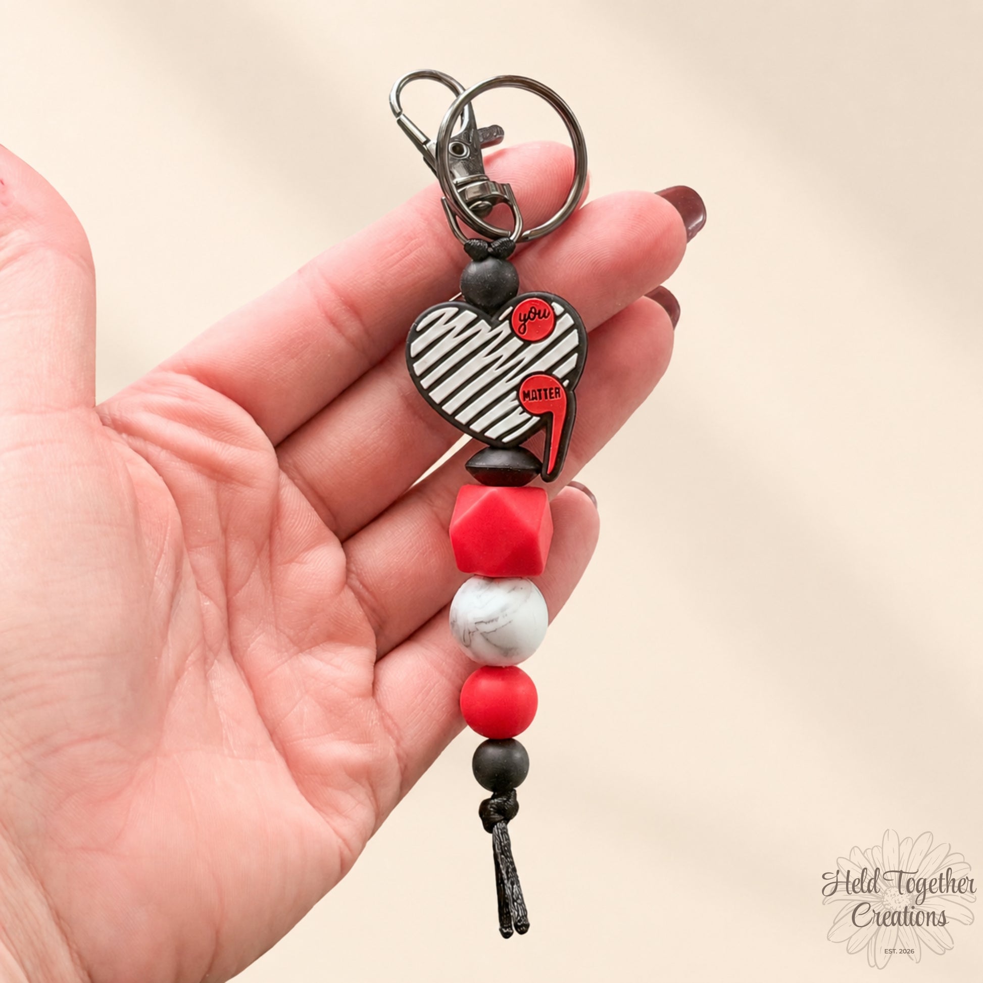 Heart-shaped keychain with beads held in a hand against a beige background